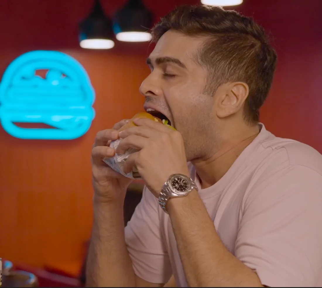 A man biting into a burger under a neon burger sign