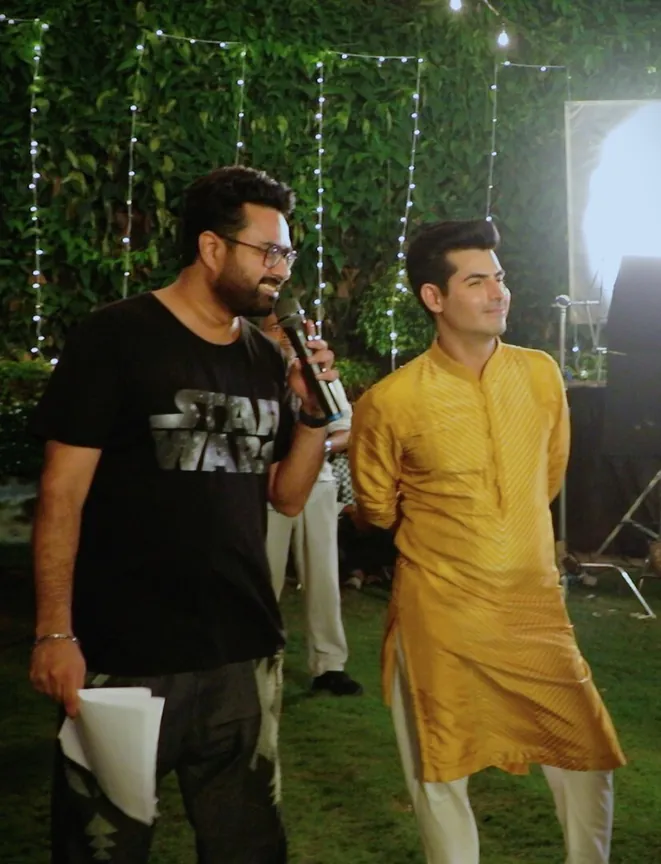 Dinesh with an actor in a yellow kurta on a garden set at night